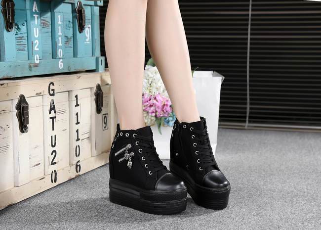 Black skull zipper high-top sneakers shown from the front beside stacked trunks and flowers.
