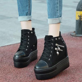 Black platform sneakers with skull zipper details worn with rolled-up jeans, viewed from above at a slight angle.