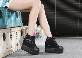 Black skull zipper platform sneakers worn in a seated side view near stacked trunks and a flower box.