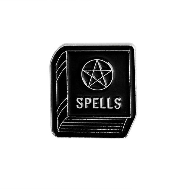 Black rectangular spellbook enamel pin with silver-tone cover lines, the word Spells and a central pentagram.