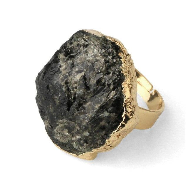 Close view of a dark stone ring with gray reflections across its irregular face and a gold-tone outline.