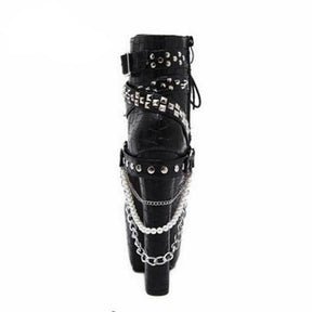 Rear view of a black reptile-textured platform ankle boot, showing straps wrapped around the ankle and layered chains and pearl-like beads draped beside the heel.