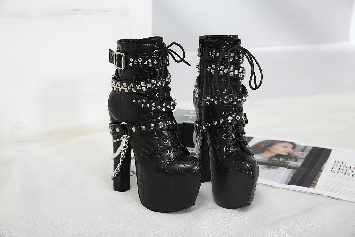 Black lace-up platform ankle boots displayed on white bedding beside an open magazine, showing their studded straps, tall heels and hanging chains.