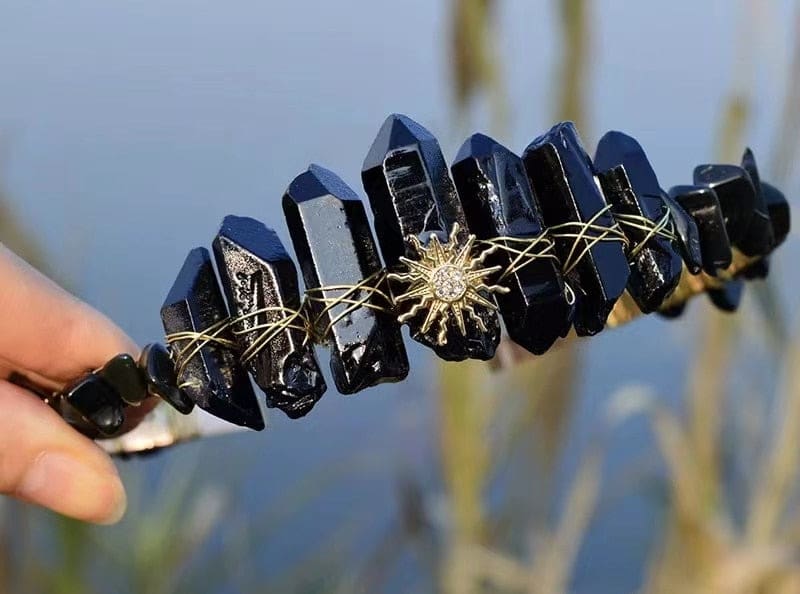 Black crystal tiara with a gold-tone sunburst at the centre, creating a sharp contrast against the dark points.