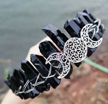 Angled view of a black crystal point crown with a silver-tone triple moon emblem and wire-wrapped band.