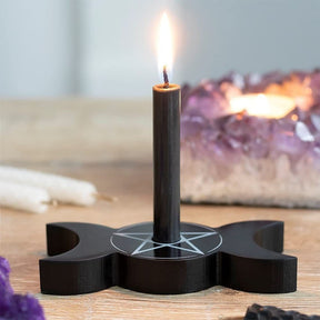 Closer tabletop view of the lit dark candle and pale pentagram on the black triple moon base, with crystals behind it.