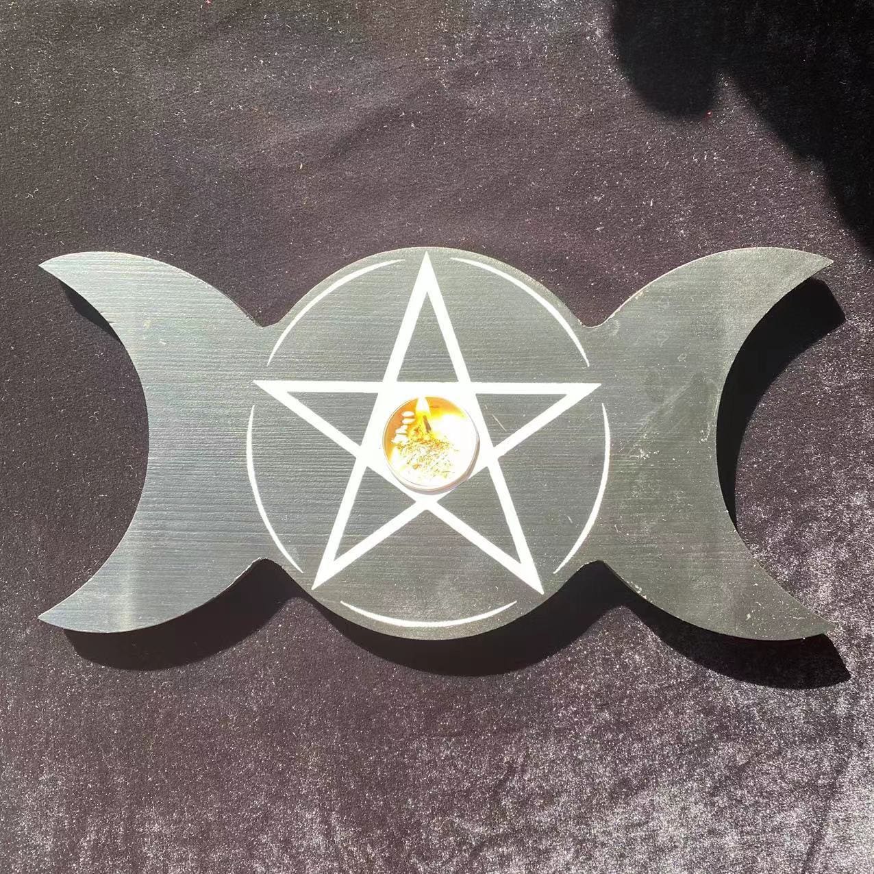 Overhead view of the black triple moon holder with a candle in its centre and white pentagram linework across the round middle.