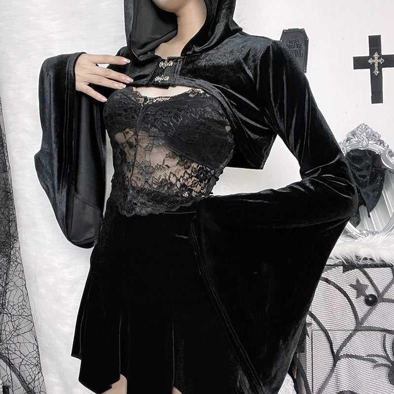 The black velvet bolero modeled with the hood raised and one arm bent, displaying a broad pointed bell cuff. A lace camisole is styled underneath.