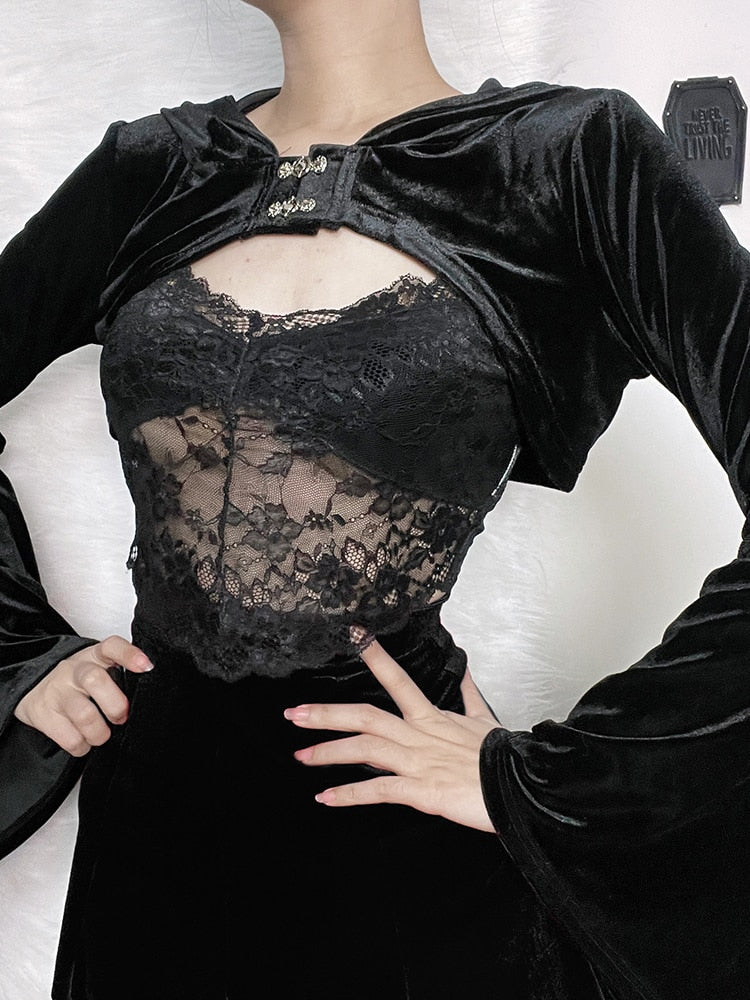 Black velvet bolero worn with the hood lowered and hands at the waist. Two decorative clasps join the cropped front above a separate lace top.