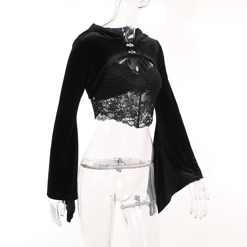 Angled view of the black velvet overlay on a clear mannequin, showing the hood, ornate clasps and flared sleeve profile over a lace camisole.