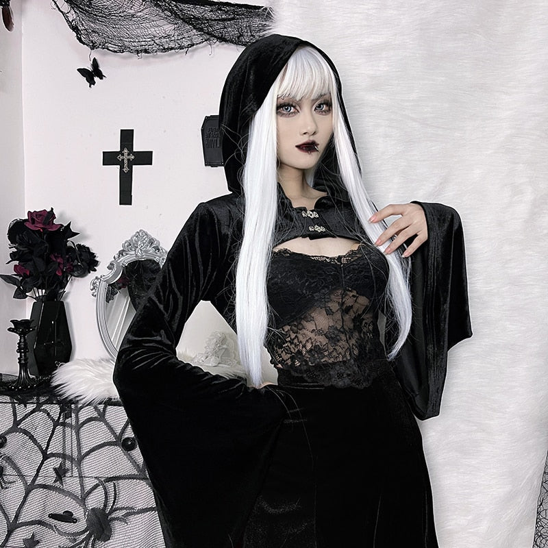 Model with long white hair wearing the hooded black velvet overlay, one hand lifted near the chest. A lace camisole and short skirt complete the styled outfit.