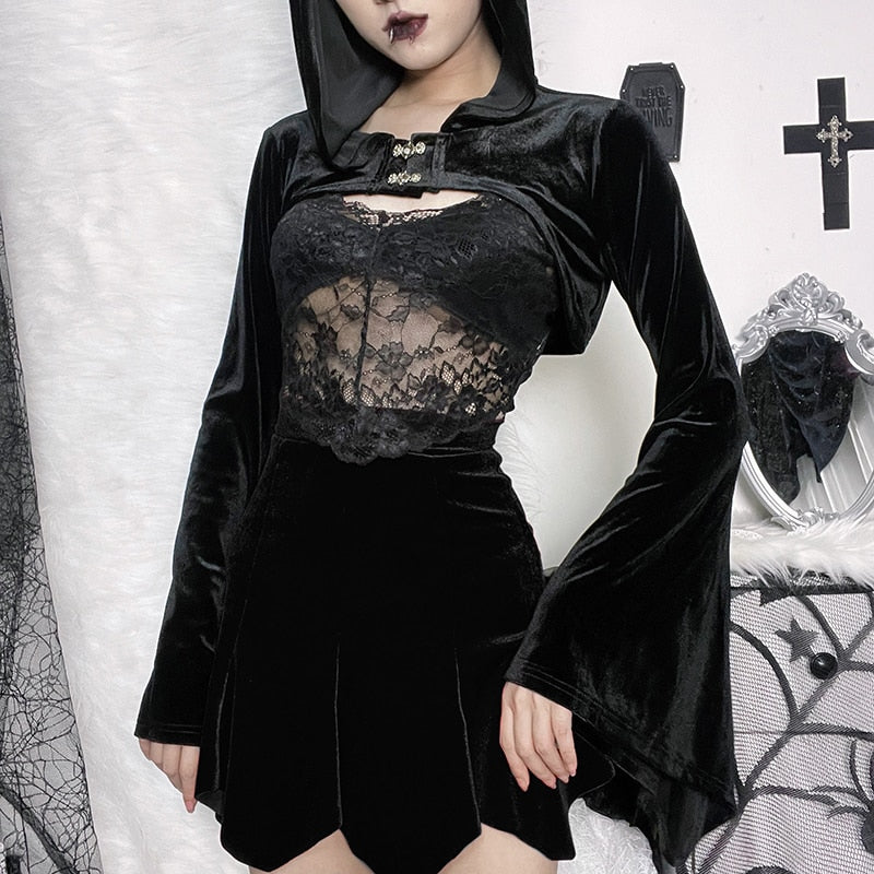 Black hooded velvet bolero shown in a gothic outfit with a lace camisole and short skirt, standing beside an ornate white mirror and dark wall decorations.
