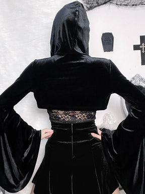 Rear view of the black velvet hooded overlay, showing its very cropped back and broad flared sleeves. A separate lace camisole and black skirt are visible underneath.