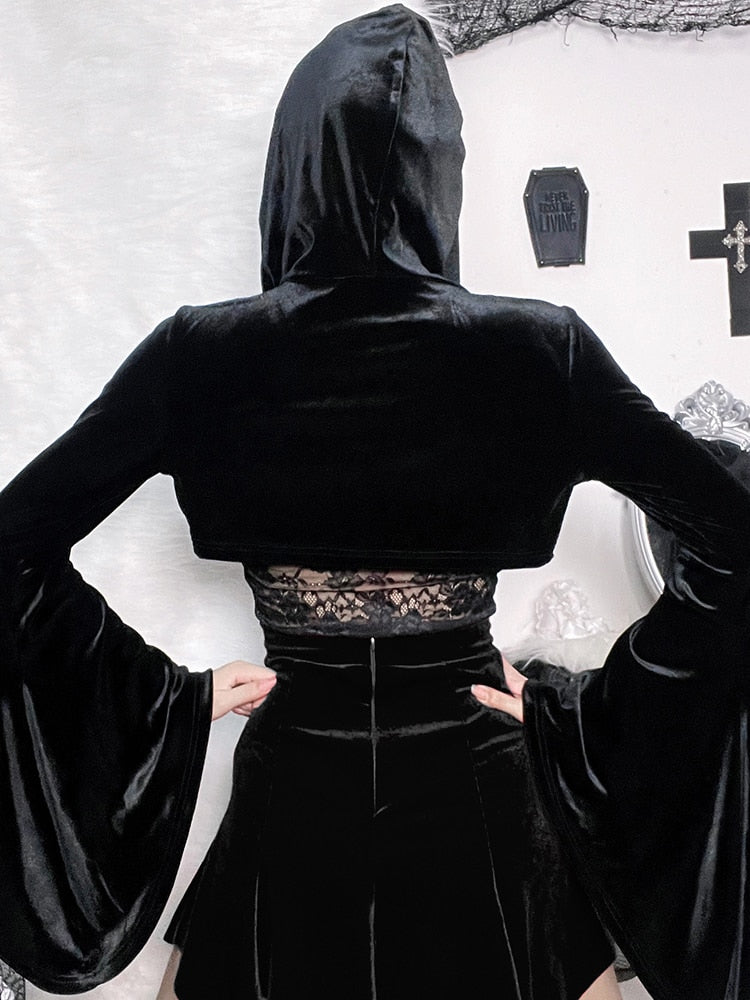Rear view of the black velvet hooded overlay, showing its very cropped back and broad flared sleeves. A separate lace camisole and black skirt are visible underneath.