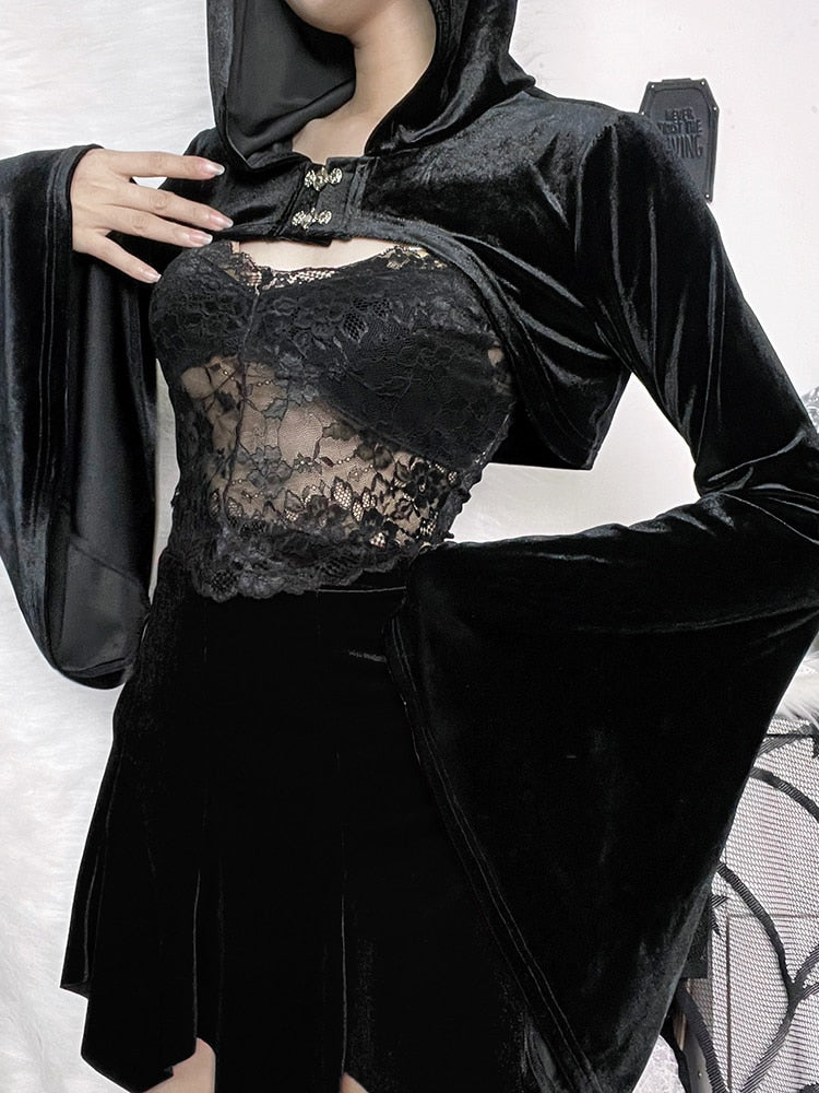 Black velvet hooded bolero modeled over a separate lace camisole, with one hand near the two ornate front clasps. Long sleeves widen into dramatic bell cuffs.