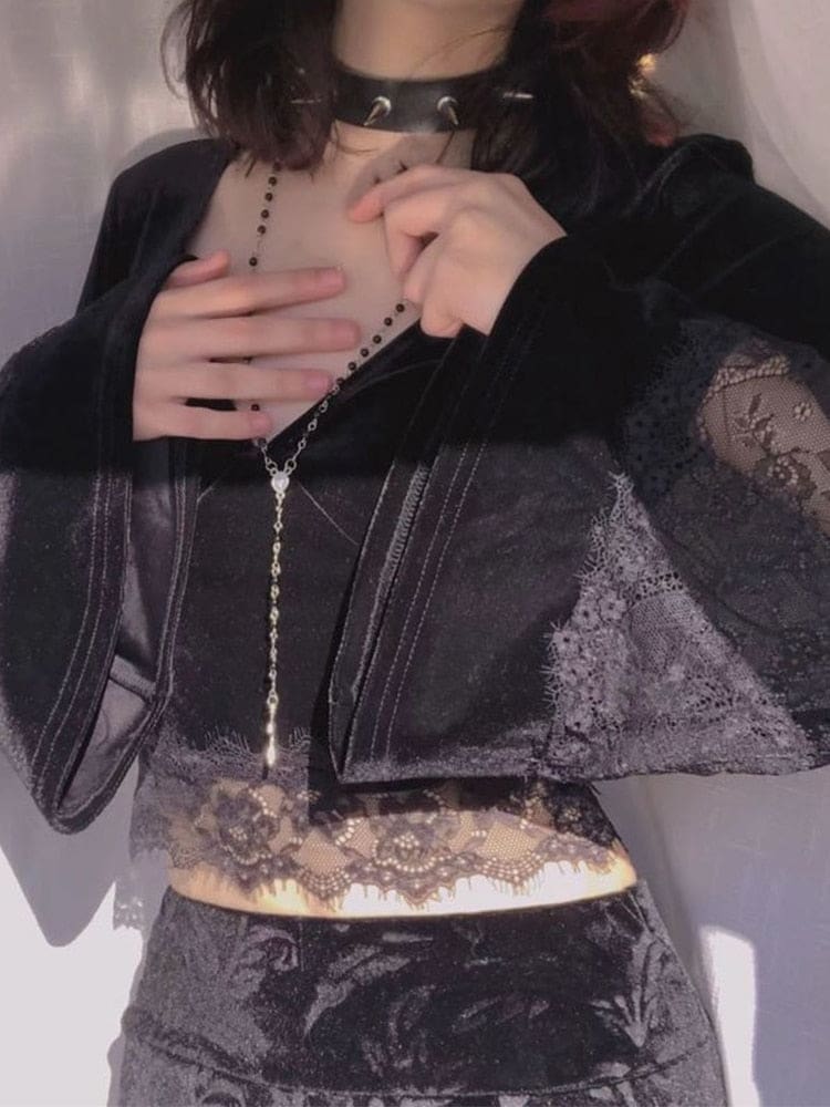Close styled view of the black velvet crop top and long lace-panel bell cuffs, with a long cross necklace hanging above the scalloped hem.