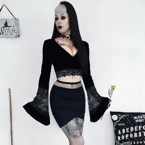 Black velvet bell-sleeve crop top styled with a fitted black skirt and patterned stockings, with sheer lace panels spanning the lower sleeves.