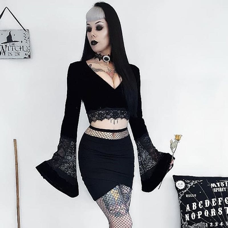Black velvet bell-sleeve crop top styled with a fitted black skirt and patterned stockings, with sheer lace panels spanning the lower sleeves.