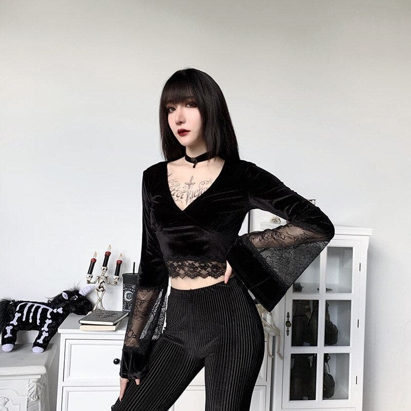 Three-quarter front pose in the black velvet bell-sleeve crop top, styled with pinstripe trousers beside white cabinets.