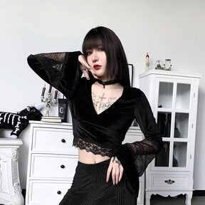 A model rests a hand near the face in the V-neck velvet crop top, with the raised flared cuff and scalloped lace waistband visible.