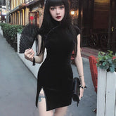 Black velvet cheongsam-inspired mini dress styled with a hand fan and dark handbag outdoors beside a storefront.