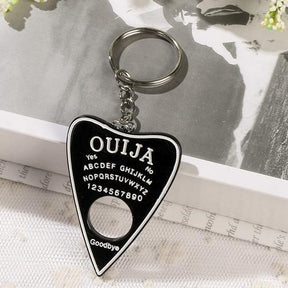 Black planchette resin keychain with a white border, alphabet and numbers, displayed on lace with its silver-tone ring resting on an open book.