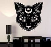 Black cat-face wall decal with pointed ears, fine fur lines and a crescent and star on its forehead. A dining-room mockup shows the design above a table.