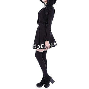 Side outfit view of the black crescent-bordered pleated skirt worn with a blouse and dark stockings.