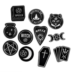 Eleven black and silver-tone witchy pin designs on white, including moons, a cat, tarot cards, a coffin, a spellbook and a planchette.
