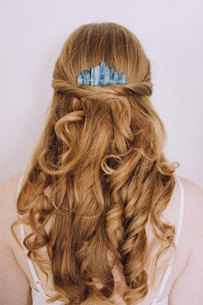 Blue crystal comb tucked into a half-up hairstyle, with the uneven stone row visible above the gathered hair.