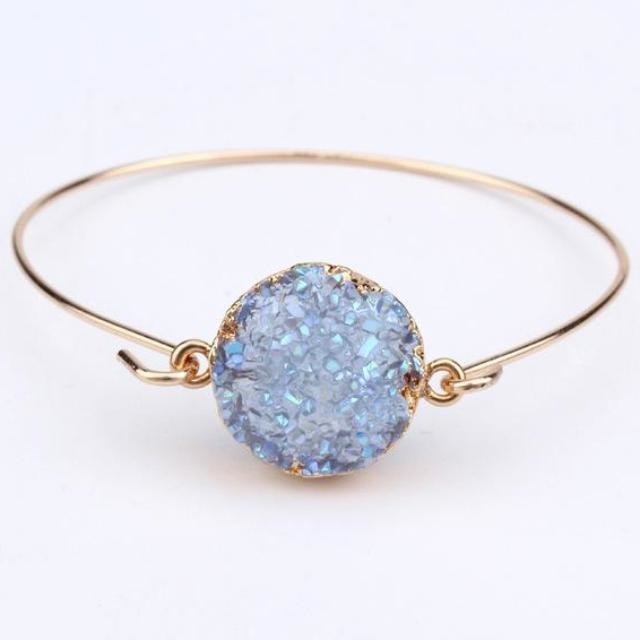 Blue druzy quartz circle cuff with an uneven glittering surface inside a gold-tone round setting.
