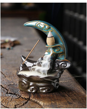 Upright Blue crescent moon burner photographed from the side-front on a wooden block, showing the gold-toned trim, curved basin and descending smoke.