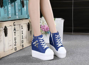 Blue and white platform wedge sneakers shown from the front beside trunks and flowers.