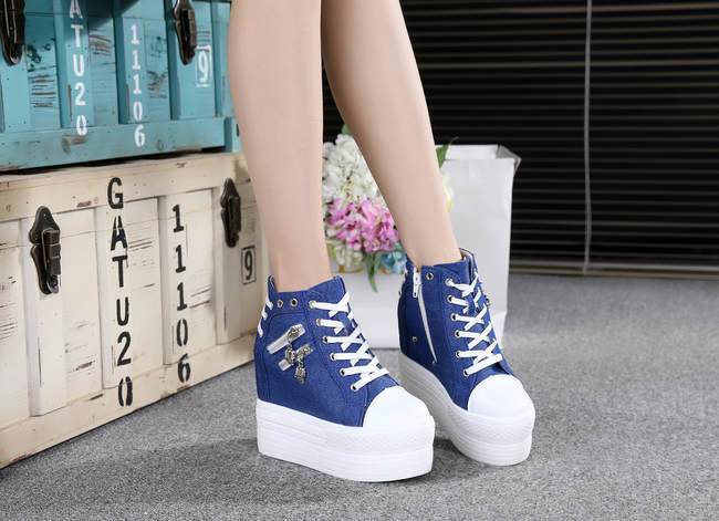Blue and white platform wedge sneakers shown from the front beside trunks and flowers.