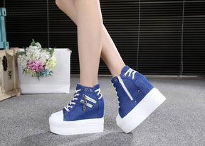 Blue skull zipper platform sneakers worn with crossed ankles, showing the outer zippers and white wedge soles.