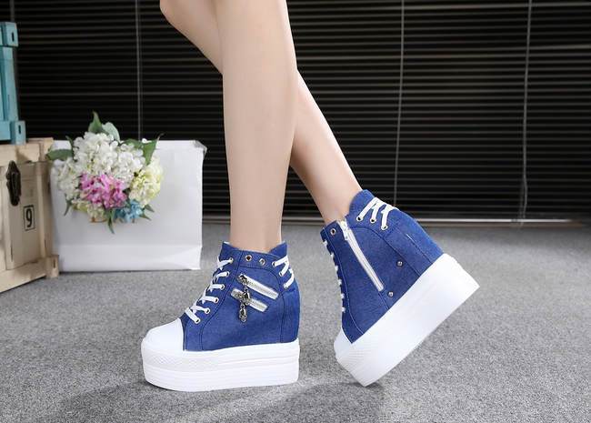 Blue skull zipper platform sneakers worn with crossed ankles, showing the outer zippers and white wedge soles.