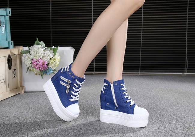Blue platform sneakers in an inner-side view, with white laces, side zippers and raised white soles.