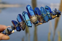 Blue crystal tiara with a pointed gold-tone sunburst emblem beneath tall blue crystal points.