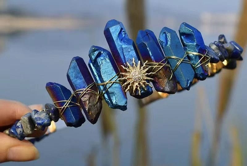 Blue crystal tiara with a pointed gold-tone sunburst emblem beneath tall blue crystal points.
