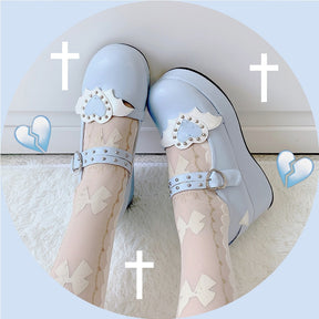 Blue winged-heart Mary Janes worn with sheer patterned stockings, photographed from above against a pale blue graphic background.