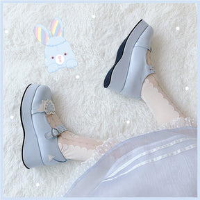 Blue winged-heart platforms worn with white stockings in a reclining pose, showing the tall sole profile and pale wing decoration.