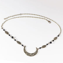 Bronze-tone crescent headdress with small black faceted beads, ornamental links and an extension chain, arranged in an oval on a pale background with the clasp and chain visible.