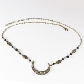 Bronze-tone crescent headdress with small black faceted beads, ornamental links and an extension chain, arranged in an oval on a pale background with the clasp and chain visible.