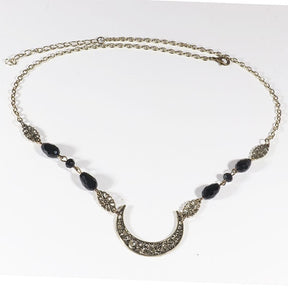 Bronze-tone ornate crescent headdress with large black teardrop beads and small dark accents, arranged in an oval on a pale background with the clasp and chain visible.