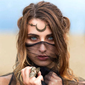 Alternate crop of a model wearing a bronze-tone crescent at the brow, with a black mesh veil across the face and a statement ring held nearby.
