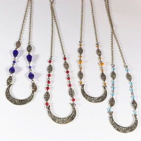 Four bronze-tone crescent headdresses hang side by side, comparing purple teardrop beads with smaller red, amber and pale blue beads.