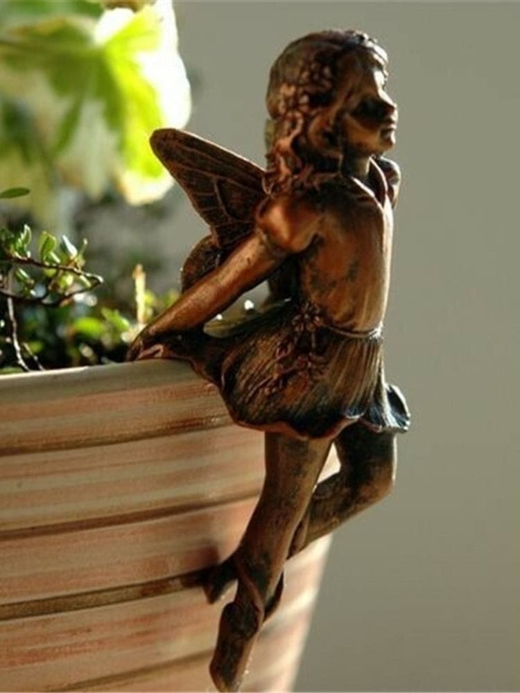 Bronze-tone seated fairy at the edge of a plant pot, with one hand near the chin and the other braced behind the petal-shaped outfit.