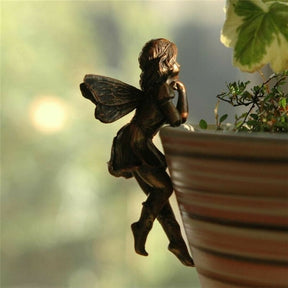 The leaning bronze-tone fairy posed at a planter edge in warm light, with one hand beneath the face and wings behind the shoulders.