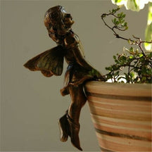 A bronze-tone fairy looks upward from the rim of a plant pot, with wings spread behind and hands resting near the edge.