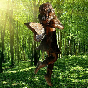 Standing fairy ornament shown against a woodland background, with folded arms, curled hair and warm metallic-tone wings.